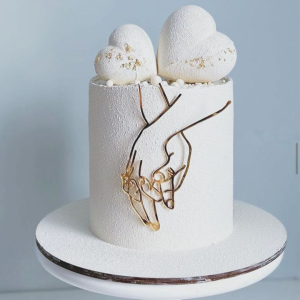 Minimalist white one-tier engagement cake with golden wire hand motif and twin heart toppers