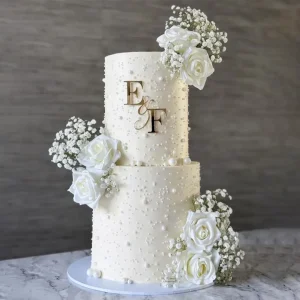Two-tier white wedding cake with pearls, white roses, baby's breath flowers, and personalized alphabet monogram topper