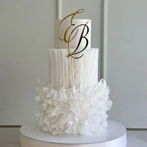 Elegant white two-tier wedding cake with delicate sugar florals and gold alphabet monogram topper