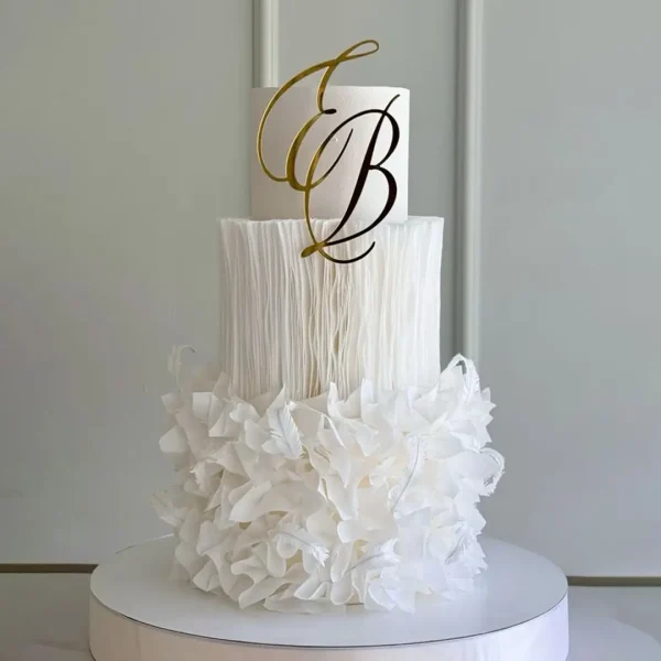 Elegant white two-tier wedding cake with delicate sugar florals and gold alphabet monogram topper