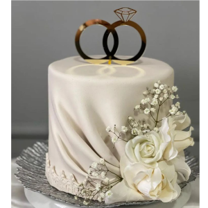 One-tier engagement cake with gold ring topper, white fondant drape, and floral decoration