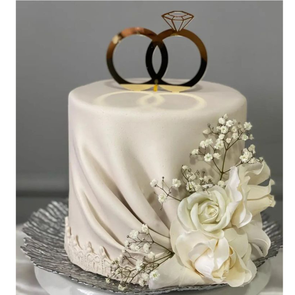One-tier engagement cake with gold ring topper, white fondant drape, and floral decoration