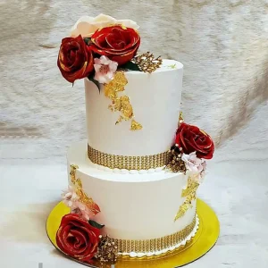 Elegant two-tier wedding cake with red roses, gold leaf accents, and gold pearl band detailing