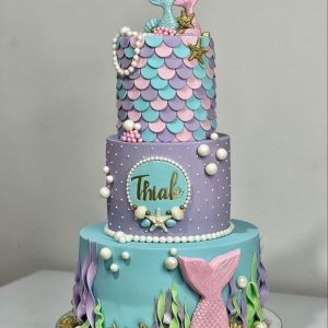 3-tier mermaid-themed cake with pastel fondant scales, seaweed, pearls, and mermaid tails on top