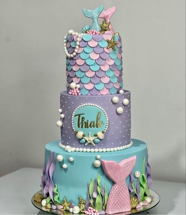 3-tier mermaid-themed cake with pastel fondant scales, seaweed, pearls, and mermaid tails on top