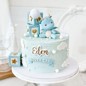 Blue dino baby cake with fondant dinosaur, balloon, clouds, and name tag for celebration