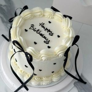 White minimalist birthday cake with black ribbon bows and small black heart decorations