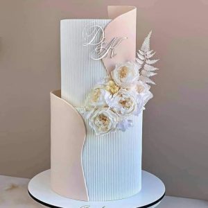 Elegant white wedding cake with vertical panel texture, blush fondant accents, and floral embellishments