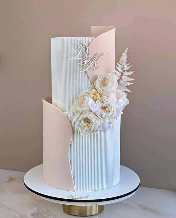 Elegant white wedding cake with vertical panel texture, blush fondant accents, and floral embellishments