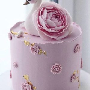 Elegant swan-themed pink cake with sugar roses and gold leaf details topped by a swan figurine