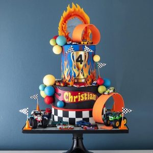 Hot Wheels themed custom birthday cake with toy race cars, flames, checkered flags, and trophy topper