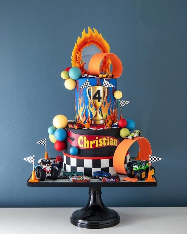 Hot Wheels themed custom birthday cake with toy race cars, flames, checkered flags, and trophy topper