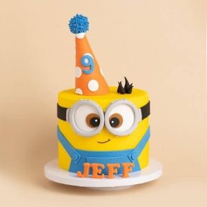 Yellow Minions-themed birthday cake with goggles, party hat, and name Jeff in fondant