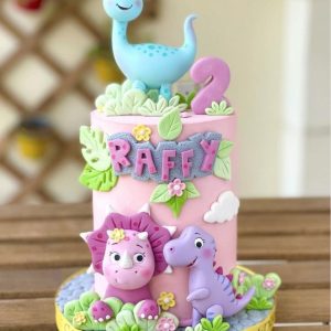 Pink dinosaur birthday cake with fondant dino toppers, name customization, and floral decorations
