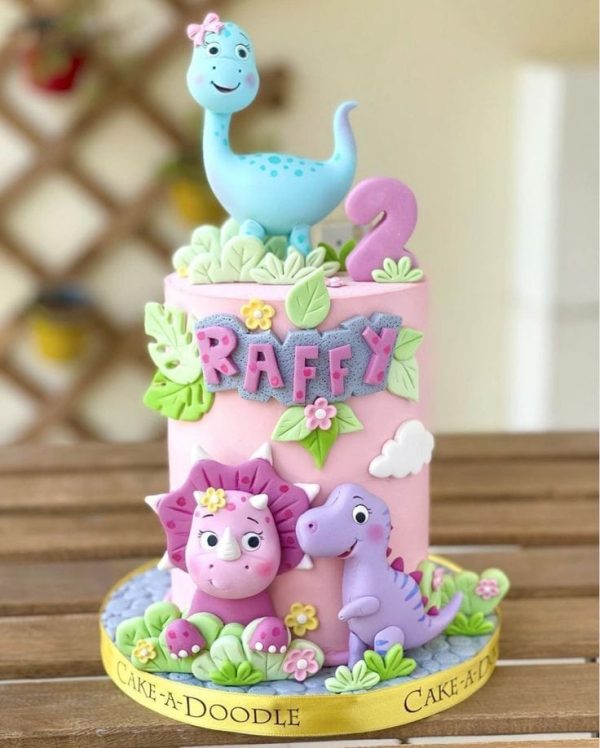Pink dinosaur birthday cake with fondant dino toppers, name customization, and floral decorations