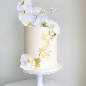 Elegant white engagement cake with edible gold leaf and white orchids on top