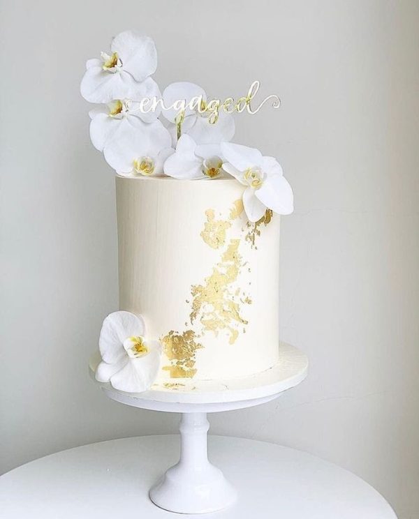 Elegant white engagement cake with edible gold leaf and white orchids on top