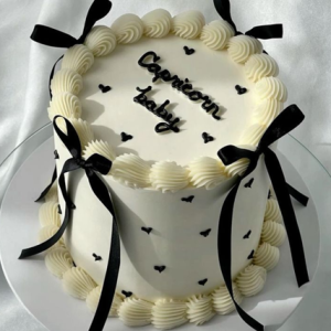 “Black and white vintage cake with piped buttercream, black ribbon bows, and ‘Capricorn baby’ message on top”